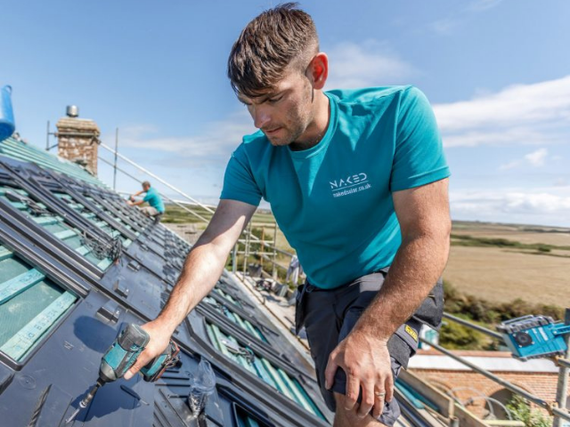 A Naked Solar installer fitting solar panels on a slate roof