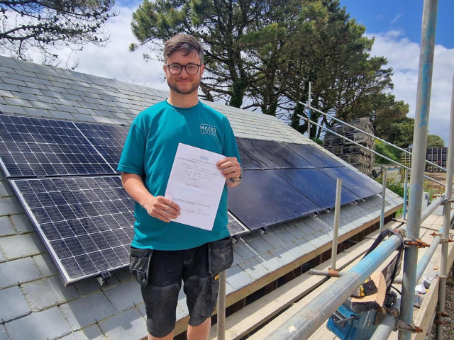 A Planet Maintenance Academy trainee holding their completed course paperwork beside a newly fitted solar array